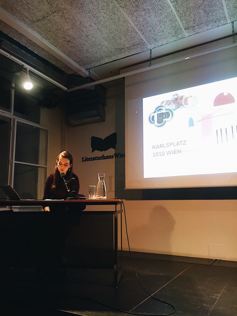 Anouk Doujak sitzt am Podium des Literaturhaus Wien und liest einen Text vor.